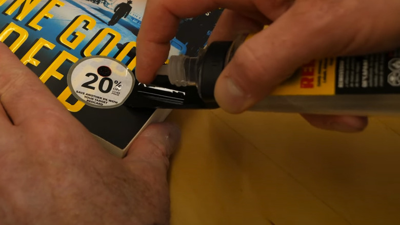 Hands using Un-Du to remove a 20% off sticker from a paper back book