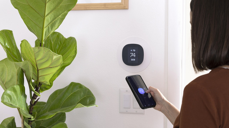 Woman using smartphone to adjust smart thermostat