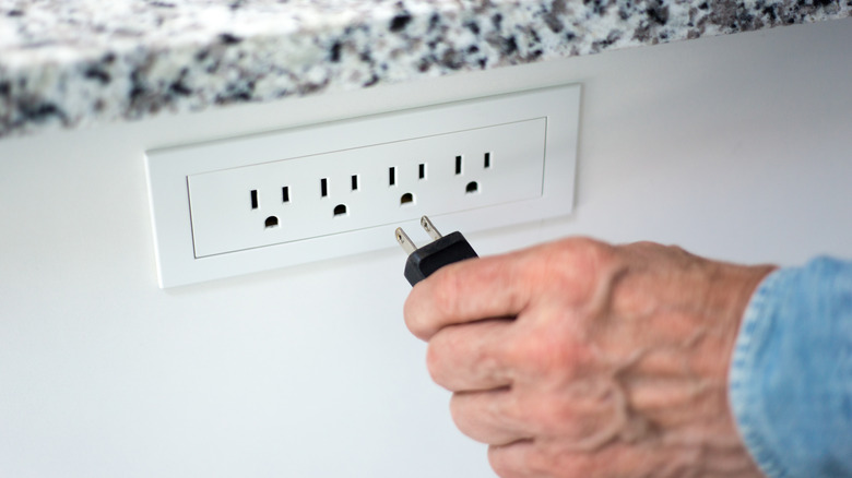 senior man plugging appliance into wall socket