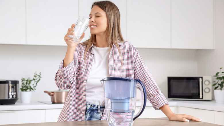 A person with a filter pitcher drinking water in kitchen
