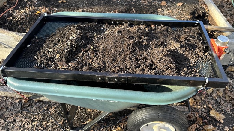 CAROD's 40W Soil Sifter on a green wheelbarrow and filled with stony soil