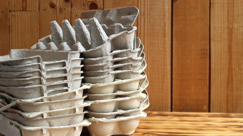 A stack of empty gray egg cartons against a wood-paneled wall