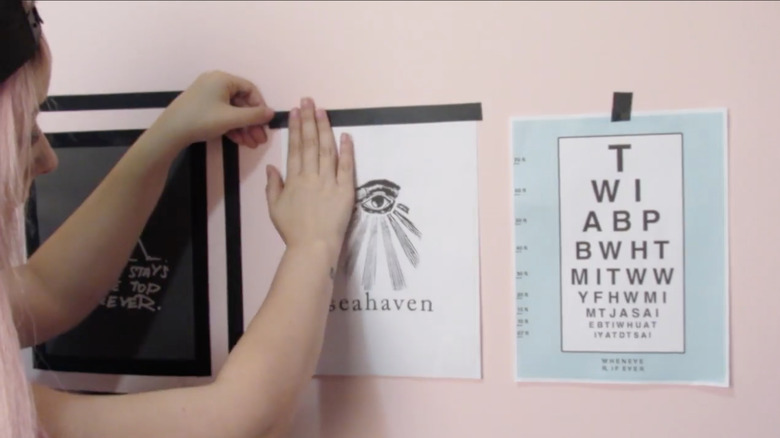 A girl with pink hair uses electrical tape to frame artwork