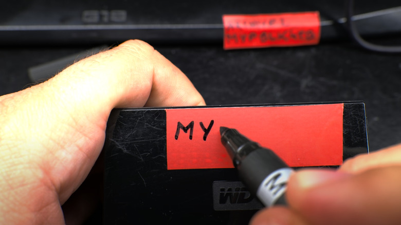 A person uses a black marker to write on a red electrical tape label