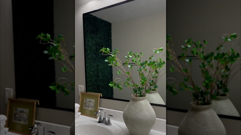 A large vase with greenery is reflected in a bathroom mirror framed with black electrical tape