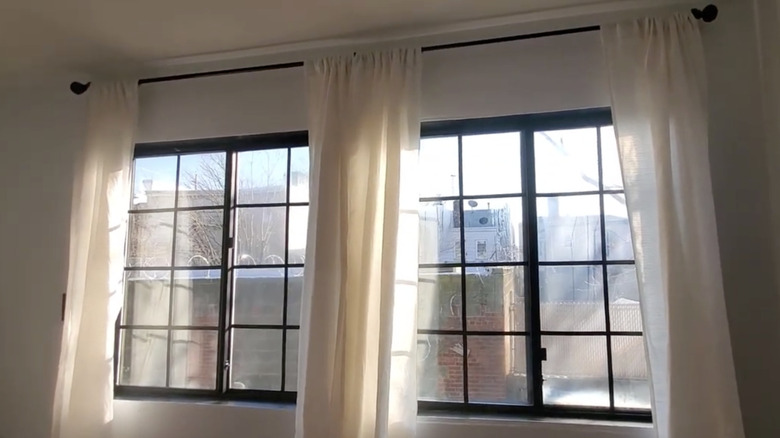 Electrical tape is used to create a grid on two light-filled windows flanked with cream curtains