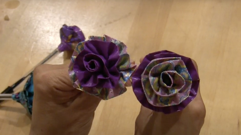 A person holds two decorative flowers made of tape