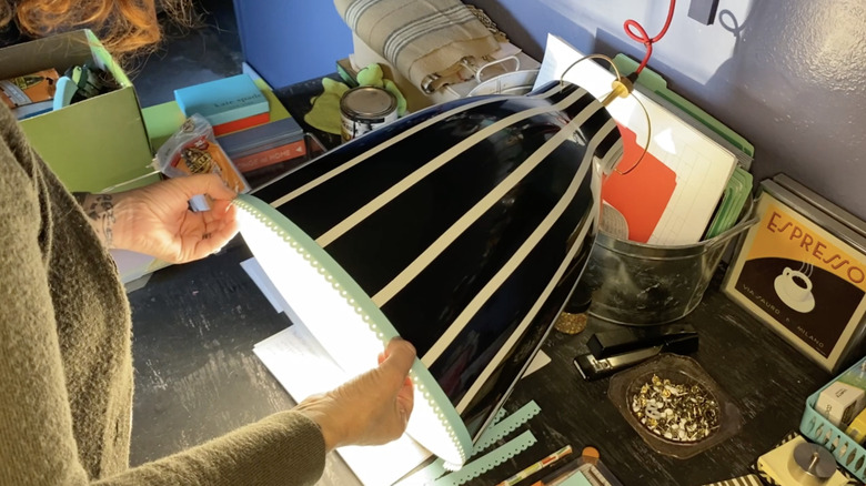 A woman attaches decorative elements to a hanging pendant light