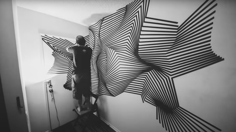 A man stands on a ladder to cover his living space with electrical tape