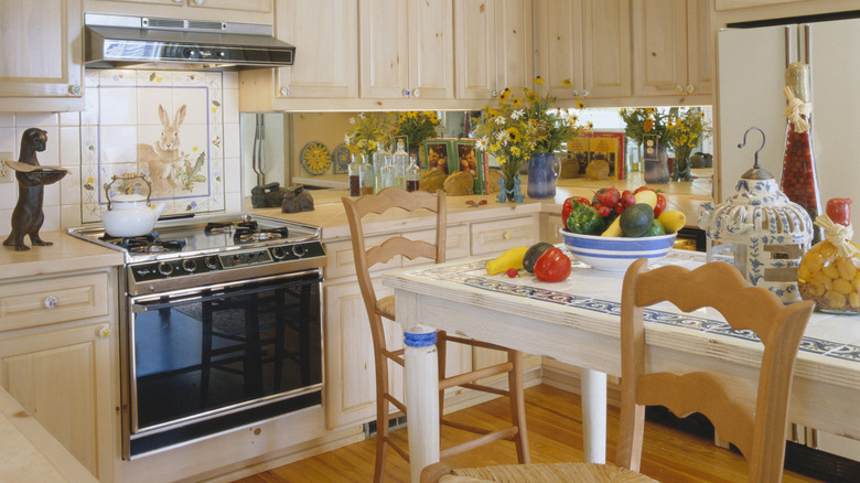 A warm and eclectic kitchen, with a mismatch of decor, an vintage kettle, and lots of flowers.