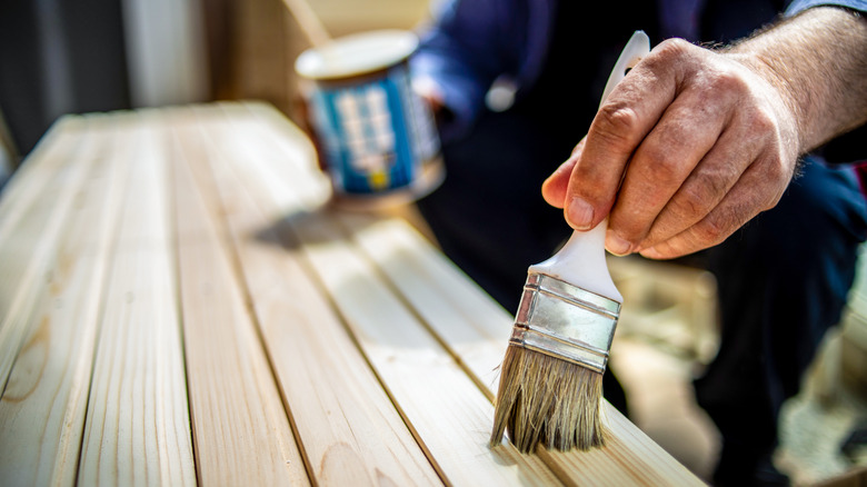 A man applies wood stain to narrow wooden slats