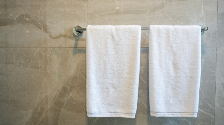 Two white bath towels hanging from a chrome towel bar.