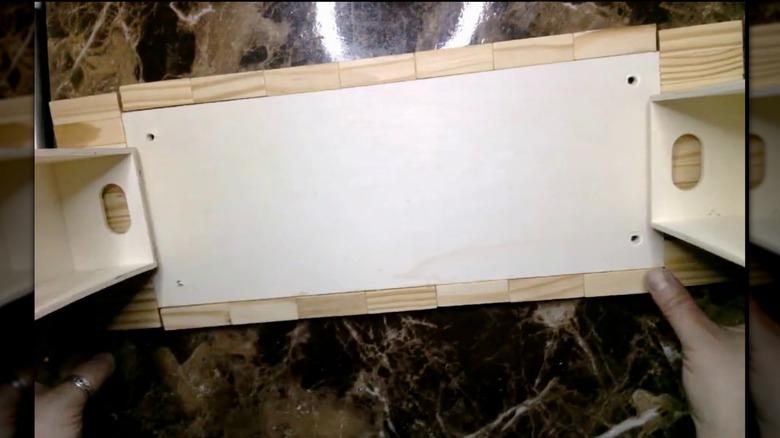 A person holds together an upside-down DIY monitor stand made of wood pieces