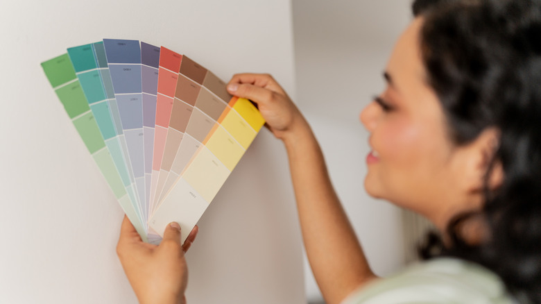 A smiling woman holding up a rainbow of paint swatches