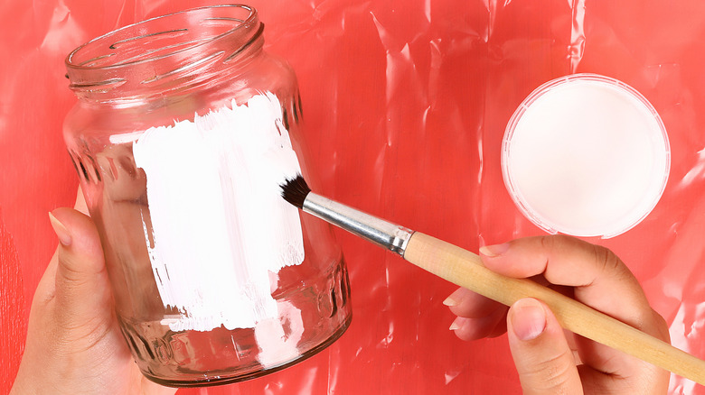 Hands painting jar white with red background behind