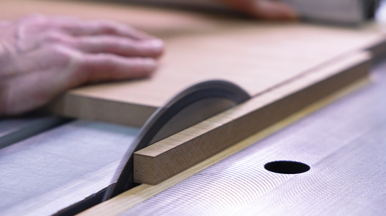 A hand cutting sheet material on a table saw