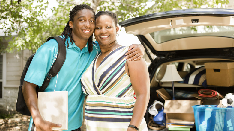 Mom and son smiling together, with son's car packed ready to leave for college