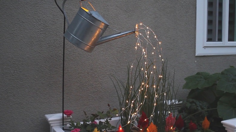 Metal watering can hanging on a shepherd's hook with fairy lights coming out of the spout