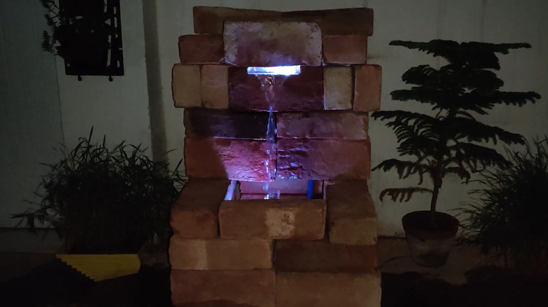Stacked brick water feature with a light in it and potted plants on the sides