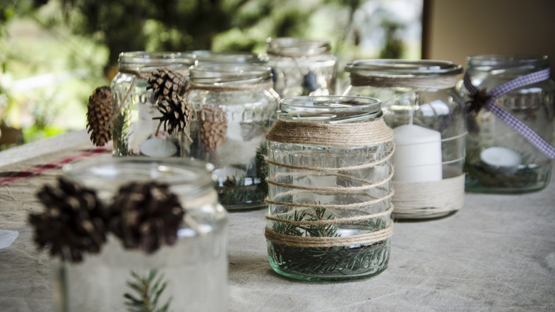 Jars containing candles, wrapped in hessian twine and decorated with pine cones and connifer sprigs.