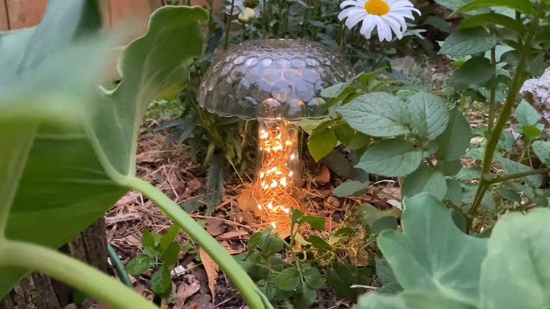 Decorative lighted garden mushroom made from a clear glass vase and bowl with fairy lights in the stem tucked into greenery