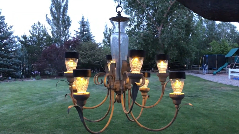 Old chandelier fitted with solar lights hanging from a tree branch in a backyard