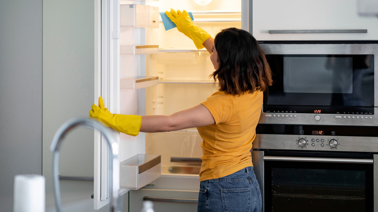 Woman cleaning shelves in fridge