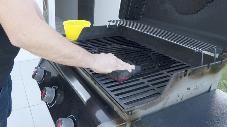 Man cleaning grill with scouring pad