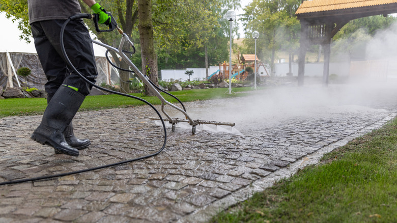 Person power washing stone driveway