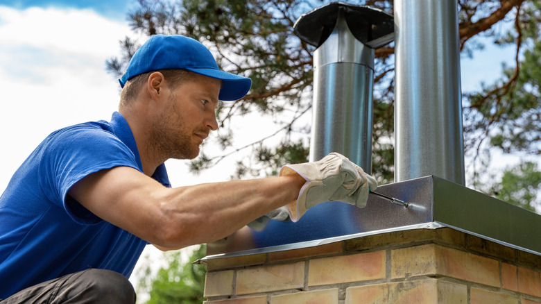 worker on the roof installing tin cap on the brick chimney