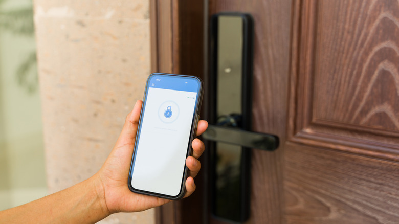 A person holds a cell phone in front of a smart lock door