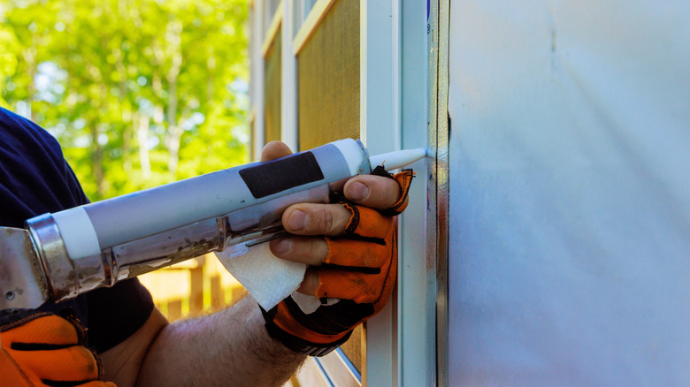 Hands coating the outside of a window with silicone weatherstripping