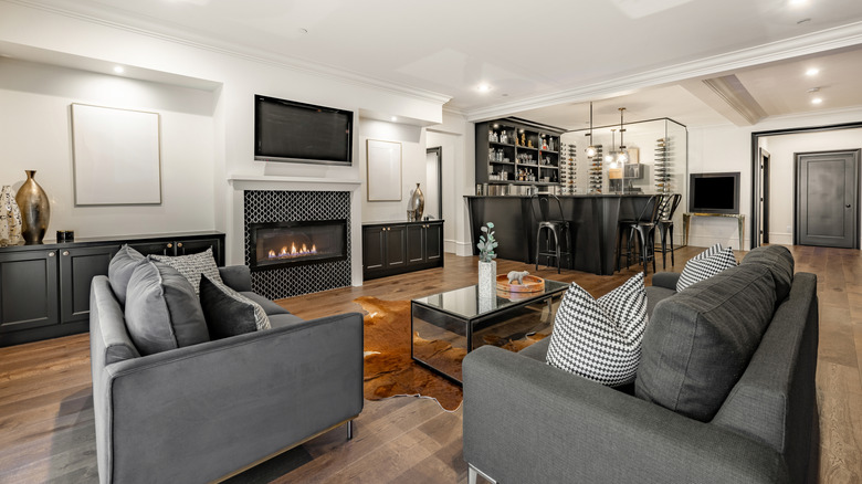 Entertainment room with sofas facing a mounted flatscreen TV with a modern fireplace underneath. A bar area and seating are in the background.