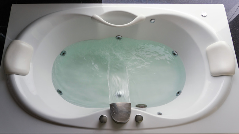 A jetted bathtub filling up with water from a waterfall faucet