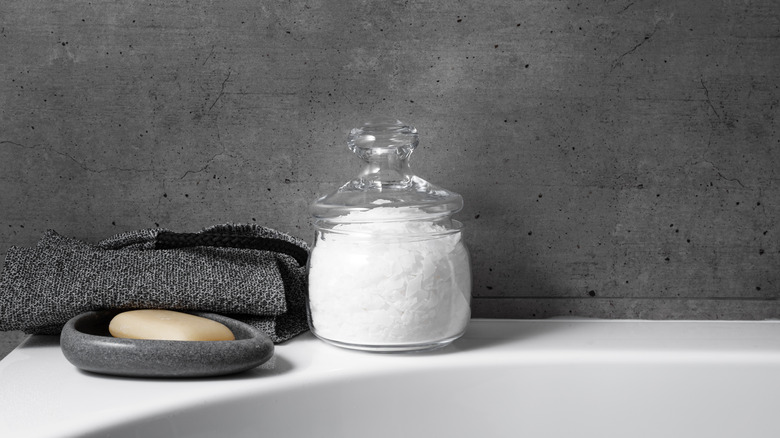 A jar of Epsom salt and a bath towel sitting on the edge of a tub