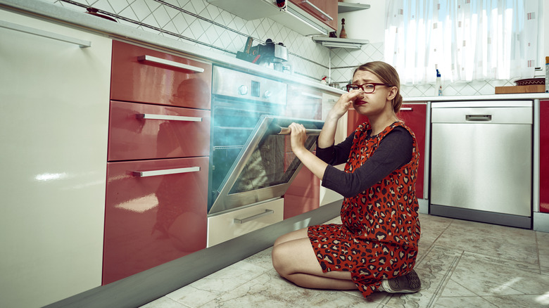 Woman plugging nose smoky kitchen