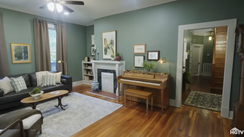 Craftsman-style living room interior with green paint, hardwood floors, black sofa, piano, and a fireplace.