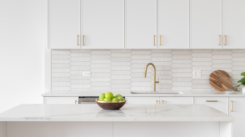all-white kitchen with white cabinets, walls and white marble countertops with gold faucets