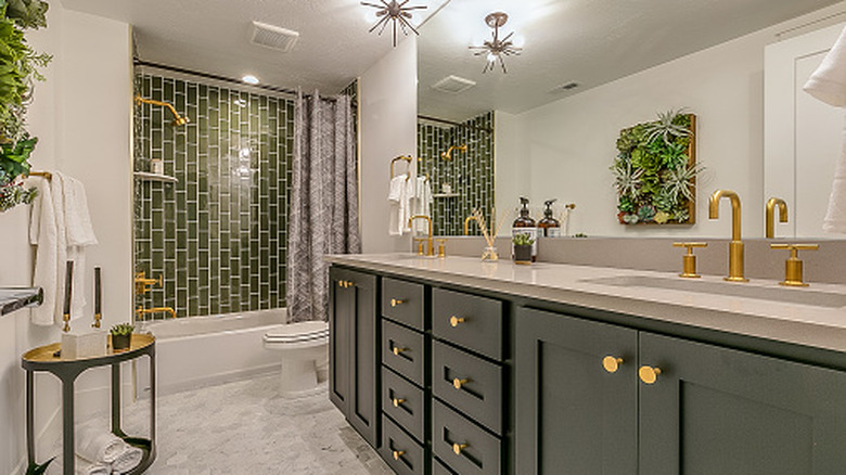 bathroom with green vanity cabinet and green tile shower with gold accents on hardware
