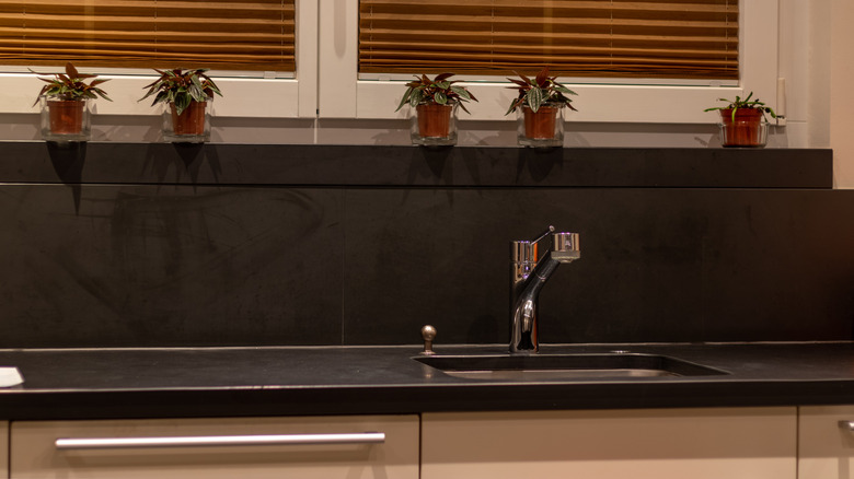 Kitchen sink with black slab countertop and backsplash