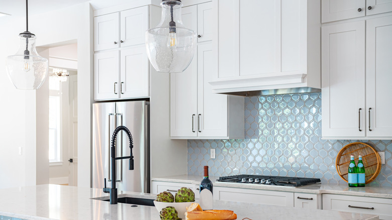 A white kitchen with light blue tile backsplash.