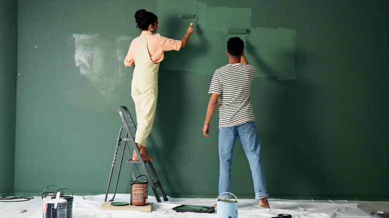 A couple painting a green wall