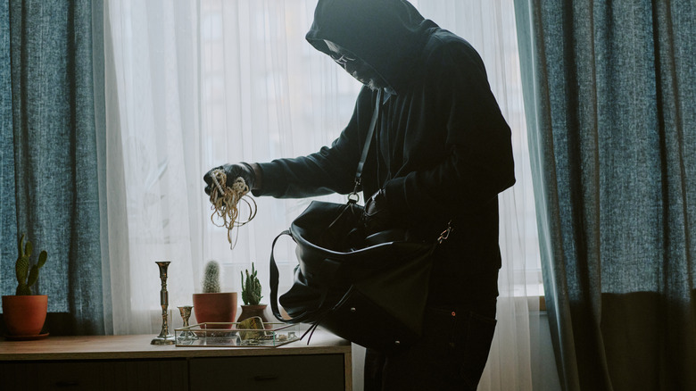Thief in black gear stealing jewelry from a home