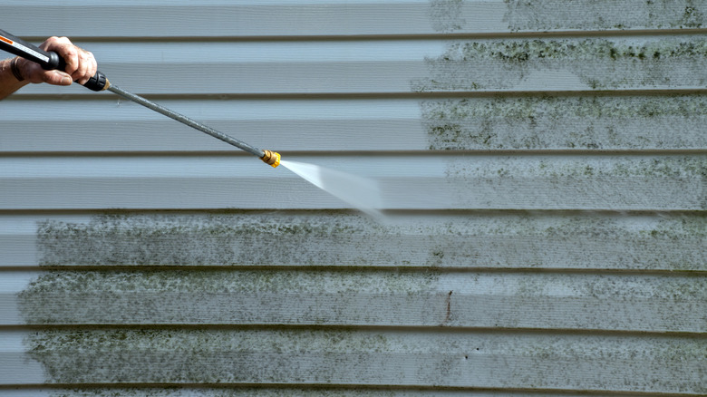 A person cleaning mold and mildew from vinyl siding with a pressure washer