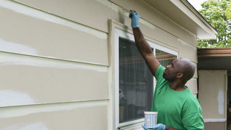 A man painting the exterior of a home with a paintbrush