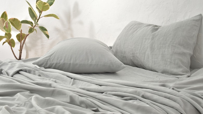 An unmade bed covered in light blue washed linen bedding.