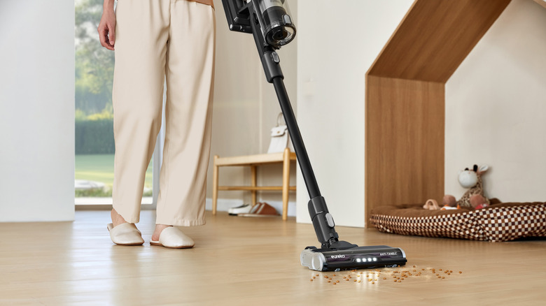 A person cleaning crumbs off of the floor with a Eureka vacuum