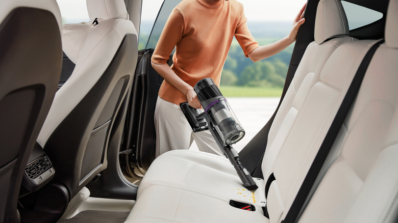 A person using a handheld vacuum to clean crumbs out of a car