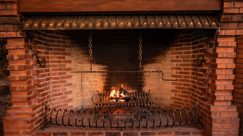 Brick fireplace with grate and metal chains for hanging pots.