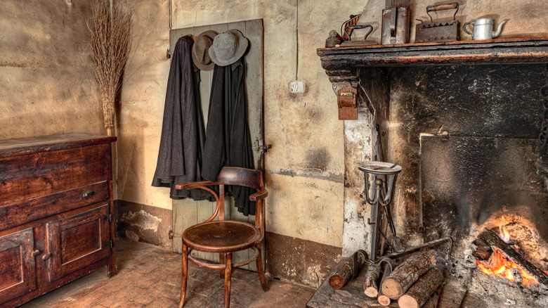 Chair next to an old fireplace with coats and hats hanging on wall.